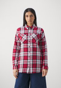 Chemise en flanelle à carreaux rouge, noir et blanc avec un devant boutonné, deux poches sur la poitrine et des manches longues. Texture lisse, motif à carreaux classique.