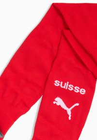 Czerwone sportowe skarpetki z teksturowanym wykończeniem, z białym napisem „suisse” oraz logo Pumy. Góra zdobiona kontrastującym szarym paskiem.