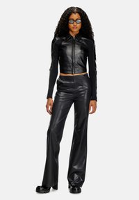 Veste courte en simili cuir noir avec fermeture éclair à l'avant et manches texturées, associée à un pantalon fluide assorti et des sandales noires à semelle épaisse.