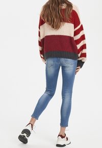 Maglione lavorato a maglia con strisce rosse e crema, orlo grigio, abbinato a jeans skinny blu e sneakers bianche con accenti rossi.