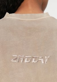 Beige sweatshirt med ribbet rund hals og tekstureret broderi af "2NDDAY" i en matchende farve på ryggen.