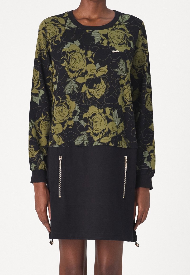 Robe noire à manches longues avec motif floral vert olive sur le haut, jupe noire unie avec deux poches zippées verticales argentées à l'avant.