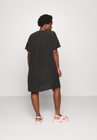 Vestido preto de manga curta com um corte relaxado, apresentando uma prega nas costas. Combinado com sandálias de plataforma de rosa claro. Textura suave.