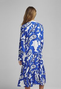 Abito a maniche lunghe blu e bianco con motivo floreale paisley, orlo arricciato e dettagli di bottoni sulle maniche, realizzato in un tessuto morbido.