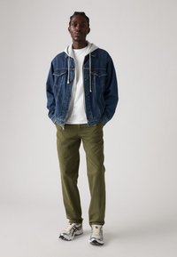 Denim jacket with two chest pockets, gray hoodie underneath, white t-shirt, olive green pants, and gray sneakers with black accents.