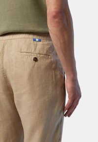Pantaloni in lino beige con una tasca posteriore, chiusura con bottone e un'etichetta di stoffa blu e bianca vicino alla vita. Finitura texturizzata.