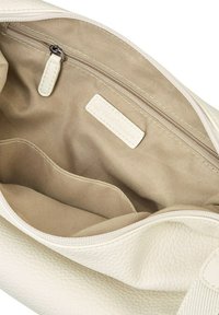 Interno di una borsa in pelle con texture crema e fodera in tessuto beige. Presenta una tasca con zip e un'etichetta cucita nella fodera.