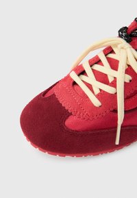 Κόκκινο αθλητικό παπούτσι με υλικά από σουέντ και ύφασμα, με στρωματοποιημένο σχέδιο, μπεζ κορδόνια και υφασμένο καουτσούκ σόλα.