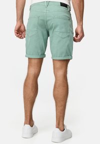 Helle grüne Jeansshorts mit umgeschlagenen Säumen, zwei Gesäßtaschen und einem schwarzen Etikett am Bund; getragen mit weißen Turnschuhen.