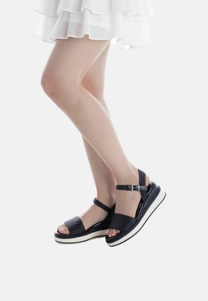 Sandali neri intrecciati con cinturino alla caviglia e fibbia, caratterizzati da una suola spessa bianca e design con punta aperta. Texture liscia e stile casual.