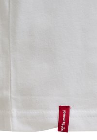 Hvid bomulds T-shirt med en syet kant og et lille rødt mærke med teksten "hummel" fastgjort nederst til venstre.