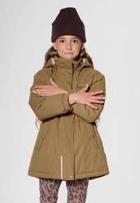 Veste isolante marron avec capuche, taille ajustable par cordon, poches latérales et fine bande d'accentuation claire ; portée avec un bonnet en tricot foncé et des leggings imprimé léopard.