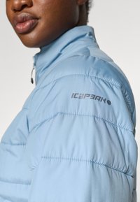 La giacca puffer azzurro chiaro presenta un colletto con zip e una texture arricciata con cuciture visibili. Include un logo "ICEPEAK" sulla manica.