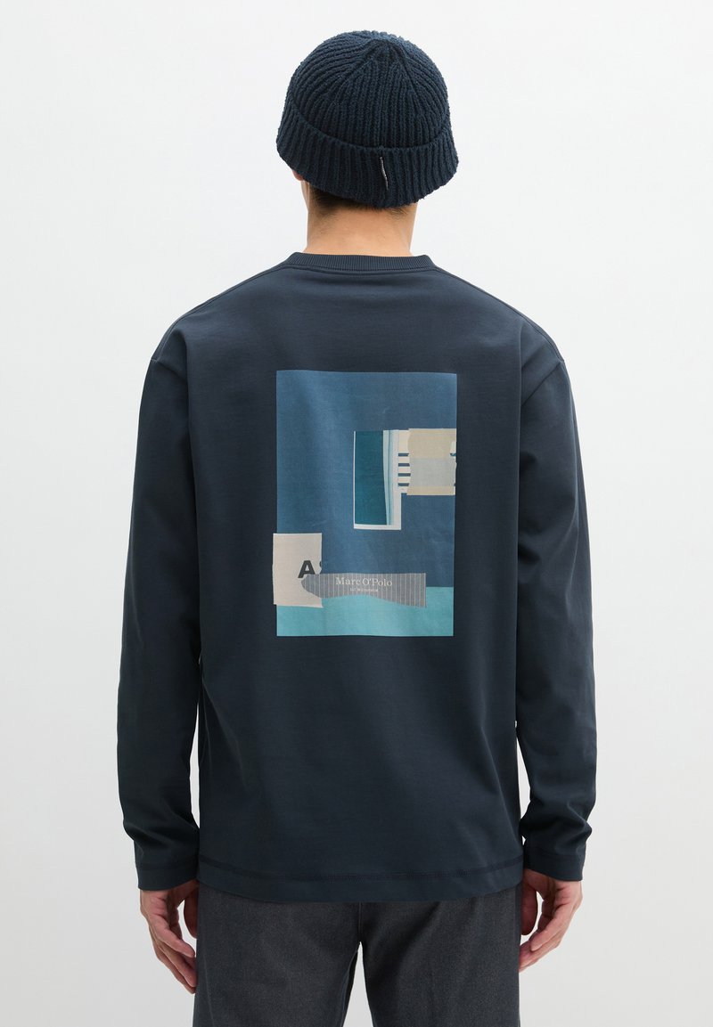 Marineblauer Sweatshirt mit langen Ärmeln und einem geometrischen Grafikdruck in Blau und Beige auf der Rückseite; verfügt über einen runden Ausschnitt und dezente Nahtdetails.