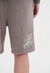 Graue Baumwollshorts mit lockerer Passform, mit gestickten Details am linken Bein und einem gesäumten Saum. Glatte Textur, mittlere Oberschenkellänge.