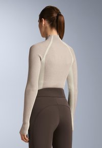 Haut côtelé beige clair à manches longues avec un col montant et un design sans coutures, associé à des leggings ajustés marron foncé.