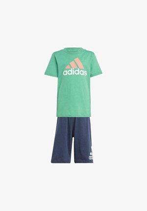 Maglietta verde in cotone con logo Adidas bianco e corallo, abbinata a pantaloni corti blu navy con un emblema Adidas bianco sulla gamba.