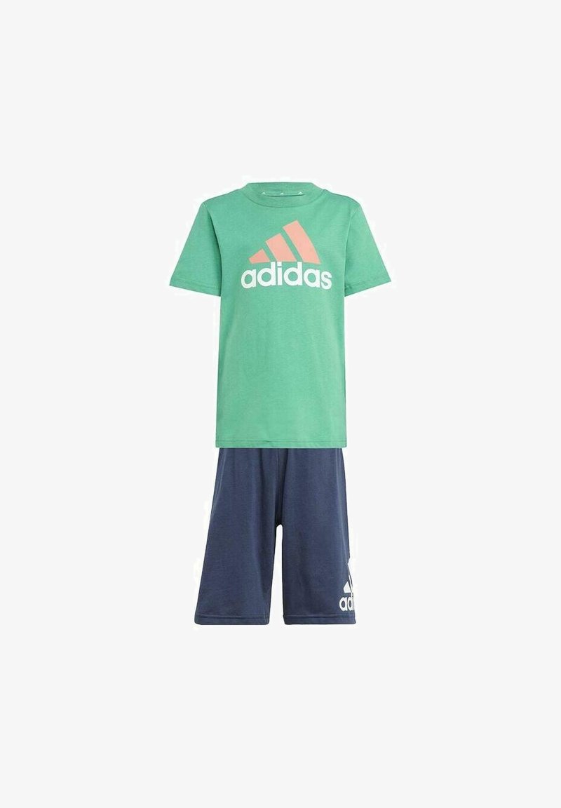Camisa de algodón verde con el logo de Adidas en blanco y coral, combinada con pantalones cortos azul marino que presentan un emblema blanco de Adidas en la pierna.