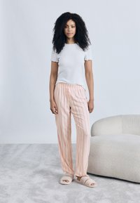Λευκή κοντομάνικη μπλούζα με ρίγες σε συνδυασμό με ροζ ριγέ παντελόνες πιτζάμας με σούρα στη μέση και κουμπιά. Ζεστές μπεζ παντόφλες τύπου slides.