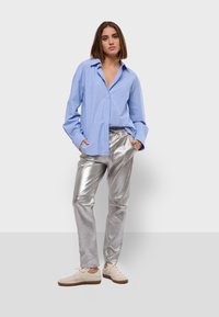 Modrá pruhovaná košile s knoflíky a límečkem, v kombinaci se třpytivými stříbrnými metalickými kalhotami a béžovými teniskami. Jednoduchý, moderní casual outfit.