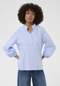 Bluza în dungi albastre și albe, cu guler tip tunică, nasturi pe partea frontală și mâneci bufante. Are o margine din dantelă de-a lungul yoke-ului.