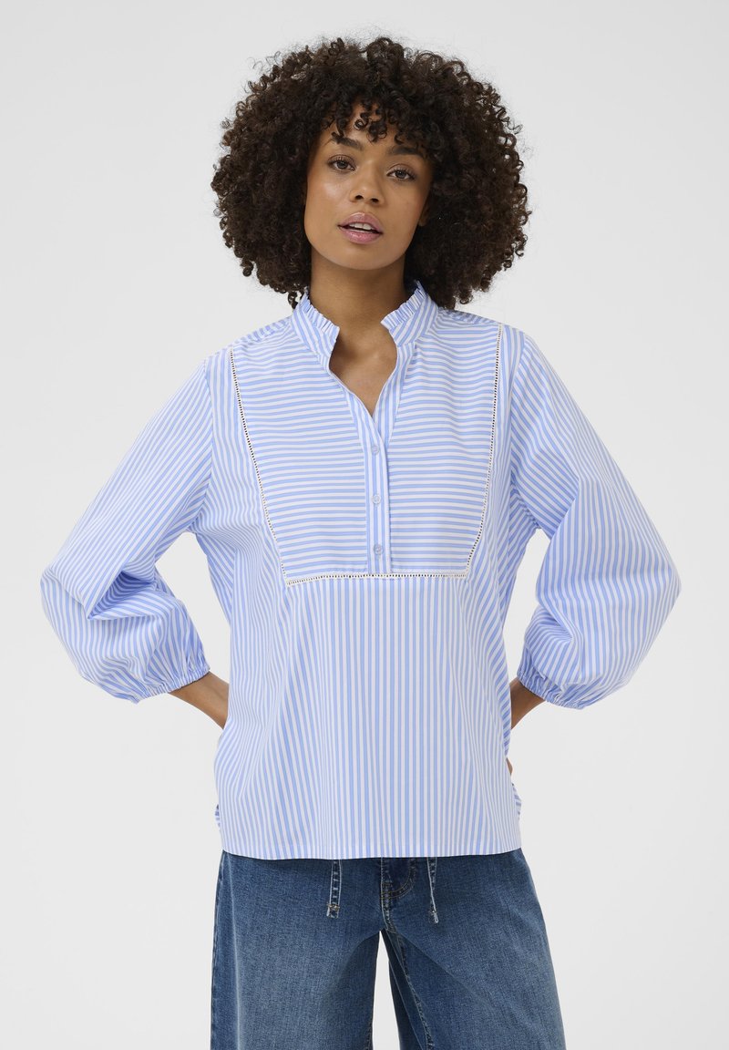 Bluza în dungi albastre și albe, cu guler tip tunică, nasturi pe partea frontală și mâneci bufante. Are o margine din dantelă de-a lungul yoke-ului.