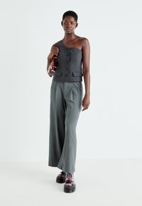 Top grigio a spalla unica con bottoni, abbinato a pantaloni larghi grigio chiaro e scarpe platform iridescenti e chunky. Piccola borsa bordeaux.