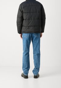 Doudoune noire avec des coutures horizontales, associée à un jean en denim bleu. La tenue est complétée par des chaussures noires et présente un design décontracté.