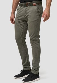 Chinos de color verde oliva hechos de una tela de textura suave, con un corte slim, bolsillos laterales y un cinturón trenzado con un acento de cuero marrón.
