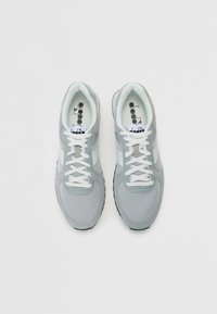 Baskets de sport gris clair avec tissu en maille, superpositions texturées et lacets blancs. Elles comportent une semelle en caoutchouc et des accents noirs au niveau du talon.