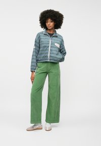 Μπλε ζακέτα με σχέδιο και φερμουάρ, με λευκή τσέπη; πράσινα καμπάνα παντελόνια από κοτλέ υλικό; γκρι και ροζ παπούτσια με λουριά; υφασμάτινη υφή.