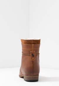 Bottine en cuir marron avec un col doux et rembourré, une ligne de couture décorative et une petite étiquette logo près du talon. Talon plat et semelle texturée.