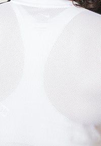 Top sportivo bianco in mesh con una texture traspirante e perforata e design arrotondato sulle spalle. Nessun motivo o colore aggiuntivo presente.