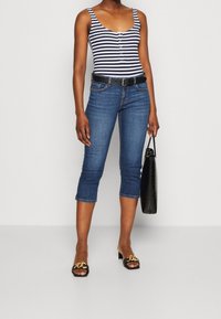 Randig ärmlös bodysuit, mörk tvättade cropped jeans, svart bälte, svart handväska och svarta sandaler med guldkedjedetalj.