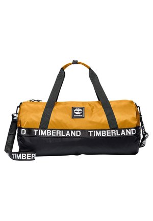 Tofarvet gul og sort duffelbag med Timberland-logo, sorte håndtag og sort skulderrem med mærke.
