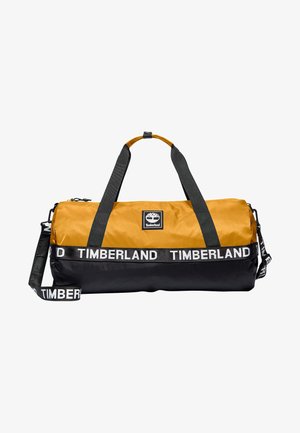 Tofarvet gul og sort duffelbag med Timberland-logo, sorte håndtag og sort skulderrem med mærke.