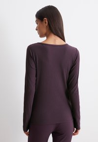 Langsleeve, paarse geribbelde shirt met een ronde hals en een getailleerd ontwerp. Zachte textuur en schone naden zichtbaar op de achterkant.