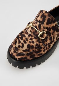 Leopardų rašto loaferiai su juodu guminiu padu, viršuje papuošti auksine detalė. Minkšta audinio tekstūra su ryškiu raštu.