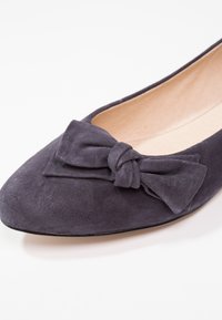 Dark purple suede flat shoe with a knotted bow detail on the front and a light beige interior lining.