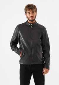 Veste en cuir noir avec col montant, fermeture éclair et poches latérales. Présente une texture lisse et une coupe cintrée.