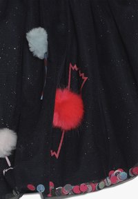 Czarna tkanina z błyszczącymi drobinkami ma białe i czerwone puszyste pomponiki oraz kolorowy cekinowy wykończenie wzdłuż dolnej krawędzi.