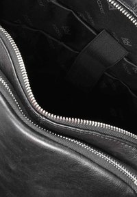 Čierna kožená taška s zipovým uzáverom. Interiér je podšitý čiernou tkaninou, na ktorej je v opakujúcom sa vzore zobrazené meno značky.