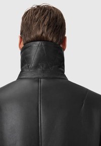 Sort læderjakke med høj krave, der har en glat tekstur og quiltet detalje på kraven. Fremstillet med præcis syning.