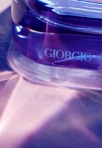 Bottiglia di profumo in vetro viola con bordi lisci e curvi e una base trasparente, caratterizzata dalla scritta "Giorgio" incisa in eleganti caratteri.