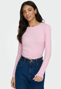 Lichtroze longsleeve top met ribbels en een ronde halslijn, gecombineerd met donkere denim high-waisted jeans en een zwarte riem.