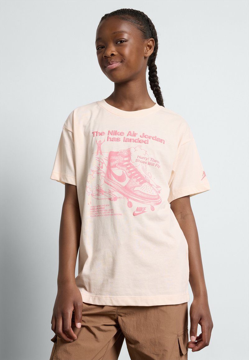 Camiseta de algodón color beige claro con estampado gráfico rosa de zapatillas y texto. Corte holgado, mangas cortas, escote redondo.