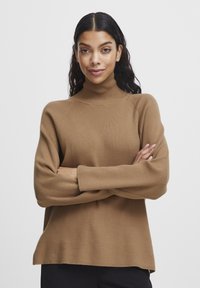 Rjava rebrasta turtleneck pulover z dolgimi rokavi in sproščenim krojem. Mehka tekstura, bočne razpoke na robu ter širši manšeti.
