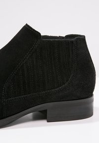 Black suede ankle boot with a textured panel, closed toe, and low stacked heel. Features a sleek, streamlined design with minimal accents.