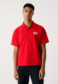 Sarkans polo krekls, kas izgatavots no kokvilnas, ar apkakli un īsām piedurknēm. Tam ir Red Bull Racing logo uz kreisā krūšu un piedurknes.