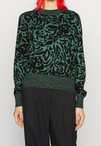 Pull tricoté vert foncé avec imprimé animal abstrait noir. Il présente un col et des poignets côtelés, un ourlet uni et un tissu texturé.